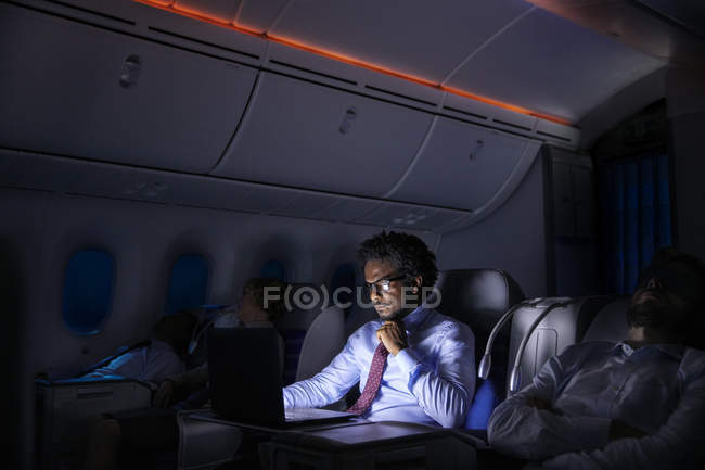 Підприємець, що працюють на ноутбук на ніч літак — стокове фото