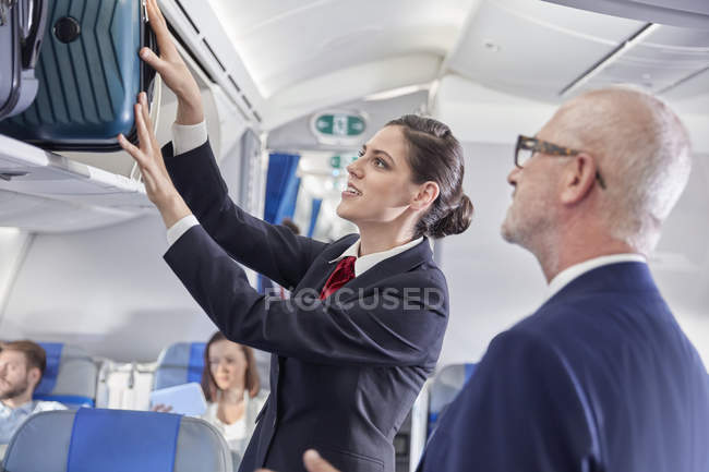 Un agent de bord aide un homme d'affaires à placer ses bagages dans le compartiment supérieur de l'avion — Photo de stock