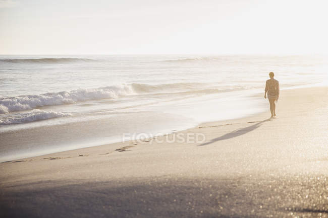 Silueta mujer caminando en idílica playa soleada de verano - foto de stock
