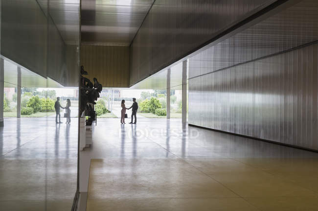 Silhouette businessman and businesswoman handshaking in modern office corridor — Stock Photo