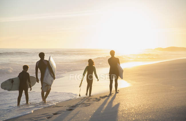 Surfistas familiares caminhando com pranchas de surf na ensolarada praia de verão ao pôr do sol — Fotografia de Stock