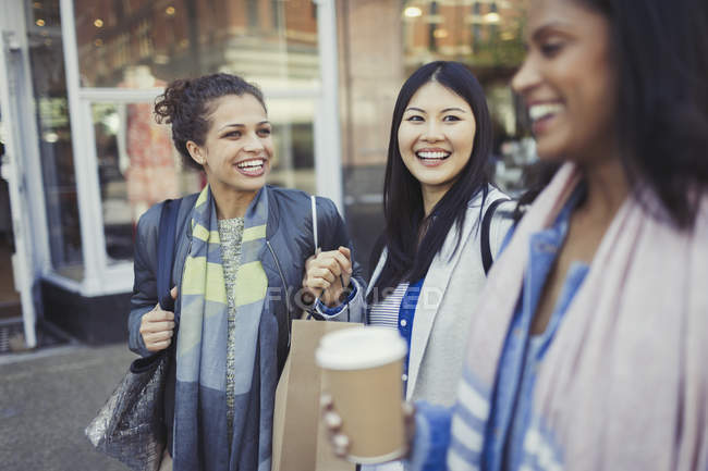 Mujeres sonrientes amigas con bolsas de compras y café frente a la tienda - foto de stock