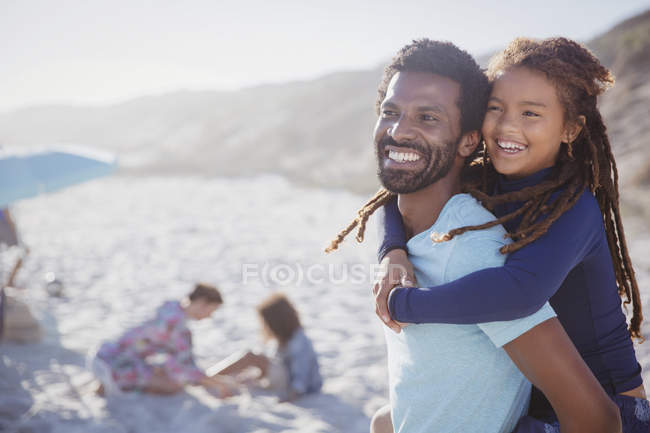 Улыбающийся, любящий отец, кормящий дочь на солнечном летнем пляже — стоковое фото