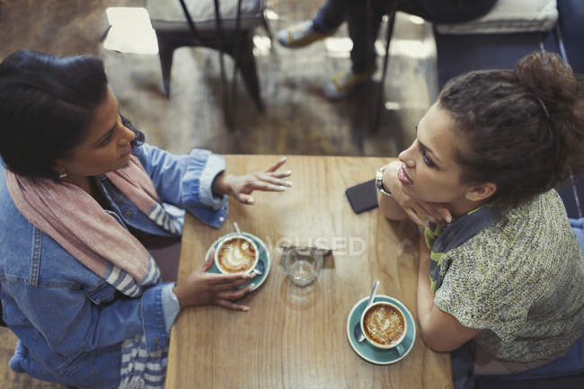 Young women friends talking and drinking cappuccinos at cafe table — Stock Photo