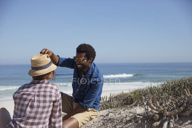 Sorrindo homem colocando chapéu na namorada na ensolarada praia do oceano de verão — Fotografia de Stock