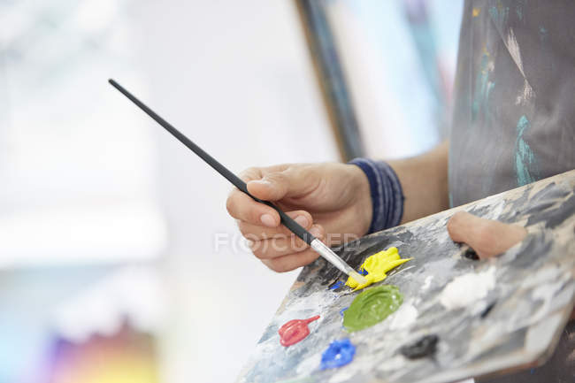 Close up artist dipping paintbrush in yellow paint on palette — Stock Photo