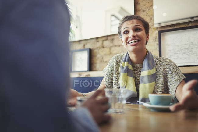 Smiling young woman talking to friend, drinking coffee at cafe table — Stock Photo