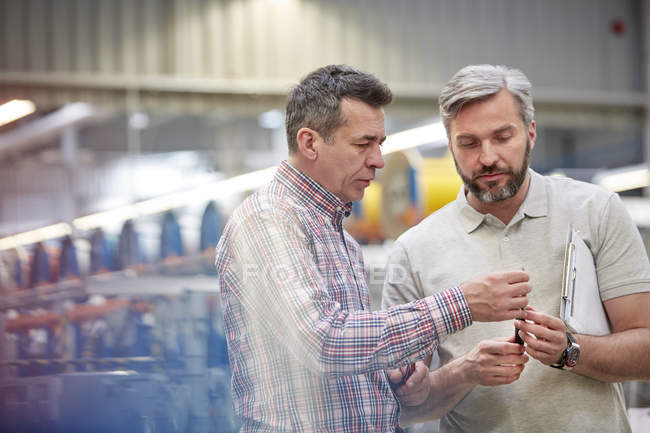 Чоловіки-робітники вивчають частину на заводі оптоволокна — стокове фото