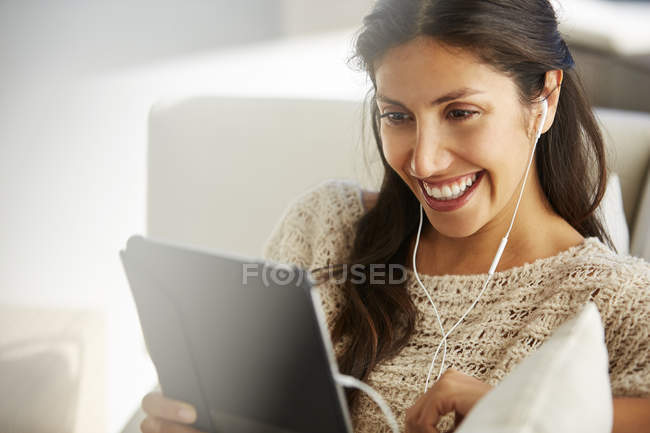 Усміхнена жінка використовує цифровий планшет з навушниками на дивані — стокове фото