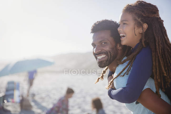 Portrait happy father piggybacking daughter on sunny summer beach — Stock Photo