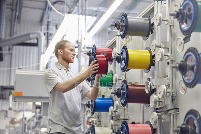 Travailleur masculin changeant les bobines sur les machines dans l'usine de fibre optique — Photo de stock