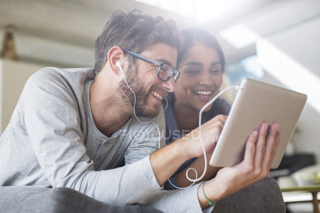 Улыбающаяся пара с наушниками с помощью цифрового планшета — стоковое фото