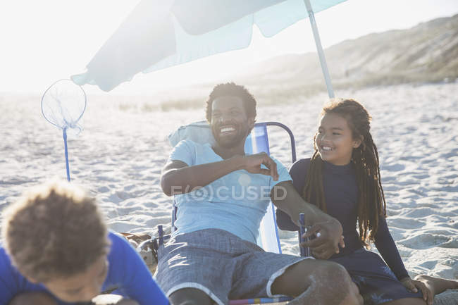 Laughing father and children relaxing on sunny summer beach — Stock Photo