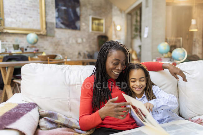 Madre e hija mirando álbum de fotos en el sofá - foto de stock