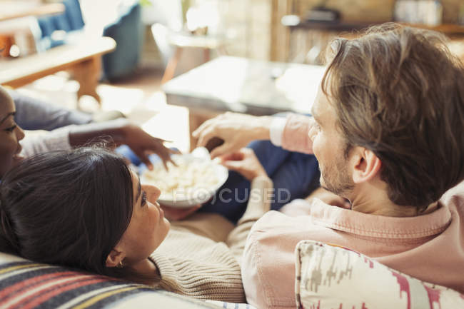 Друзі дивляться телевізор і діляться попкорном у вітальні — стокове фото