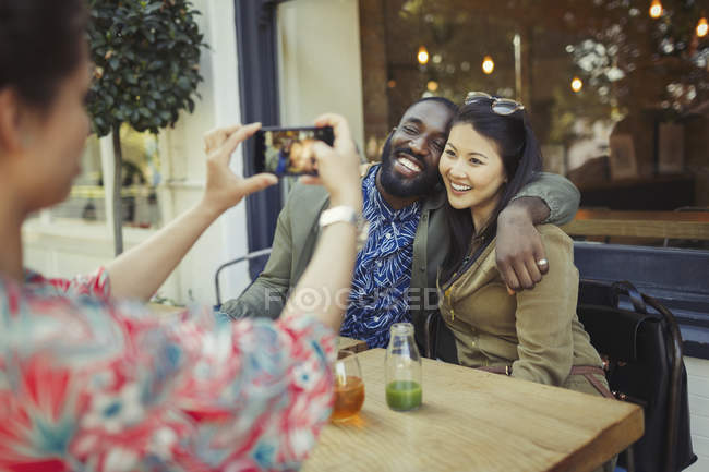 Donna fotografare affettuosi amici coppia con fotocamera telefono al caffè marciapiede — Foto stock