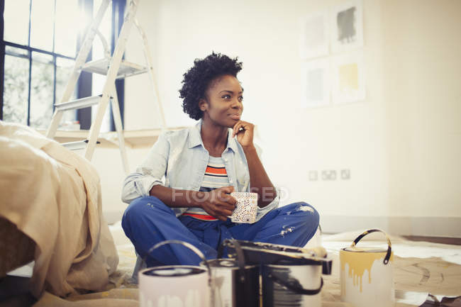 Mujer satisfecha bebiendo café y pintando sala de estar - foto de stock