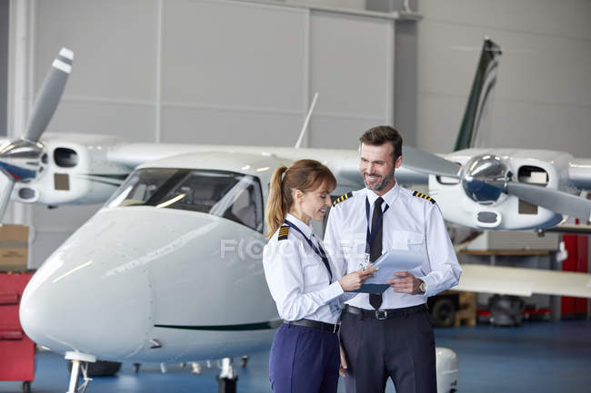 Pilotes discutant de paperasserie près de l'avion dans le hangar — Photo de stock