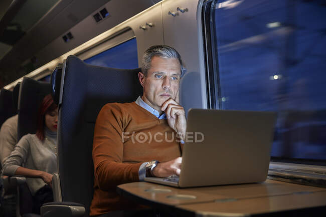 Focused businessman working at laptop on passenger train at night — Stock Photo
