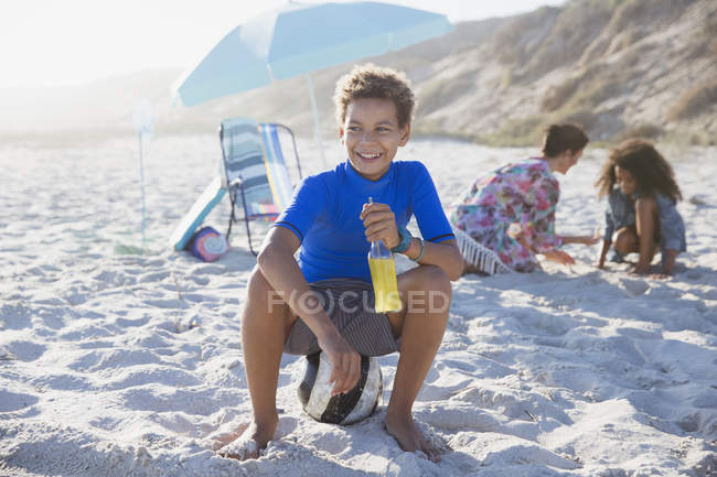 Ragazzo sorridente che beve succo sulla spiaggia estiva soleggiata — Foto stock