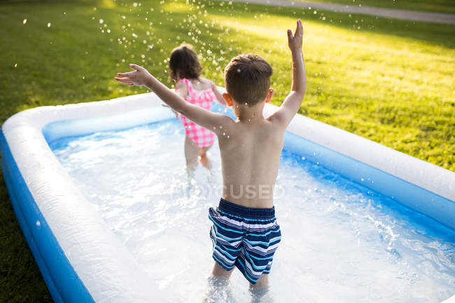 Hermano y hermana preescolares jugando y salpicando en piscina inflable - foto de stock