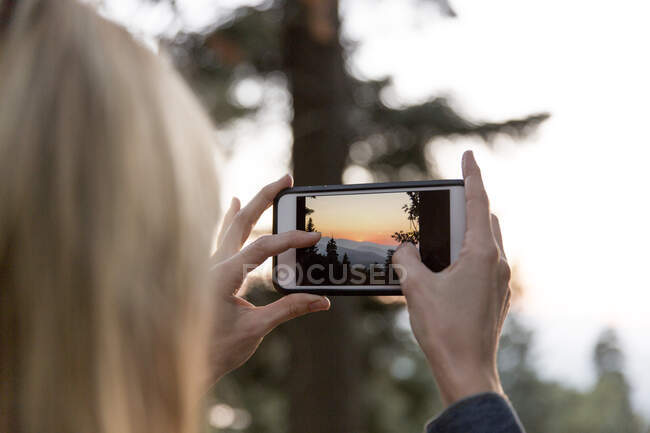 Жінка з фотоапаратом фотографує захід сонця — стокове фото