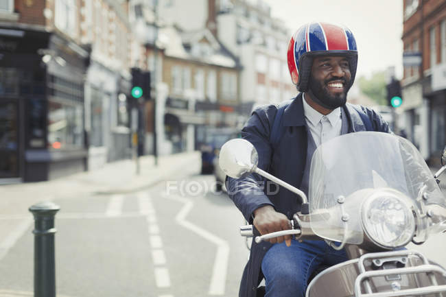 Souriant jeune homme d'affaires en casque équitation scooter moteur sur la rue urbaine — Photo de stock