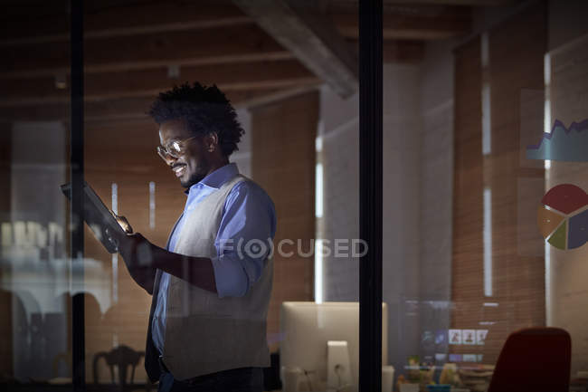 Улыбающаяся деловая женщина, работающая допоздна, использующая цифровые планшеты в темном офисе ночью — стоковое фото