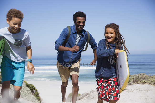 Famiglia giocosa con boogie board in esecuzione sulla soleggiata spiaggia estiva — Foto stock