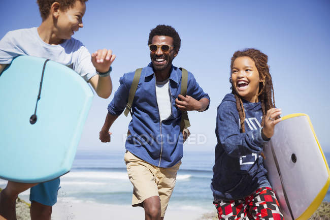 Happy father and children with boogie boards running on sunny summer beach — Stock Photo