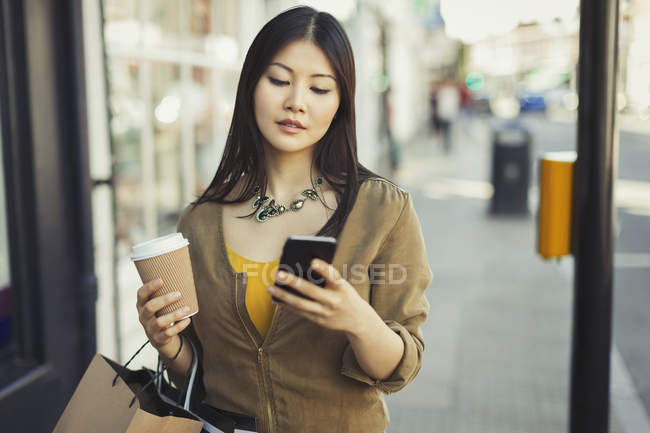 Молодая женщина с кофе смс с сотовым телефоном на городской тротуаре — стоковое фото