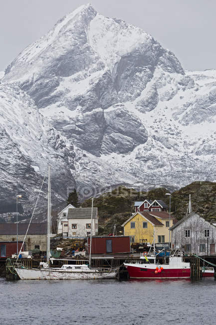 Fishing village and boats at waterfront below snowy, rugged mountains, Sund, Lofoten, Norway — Stock Photo