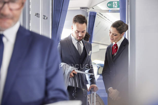 Flight attendant helping businessman with boarding pass on airplane — Stock Photo