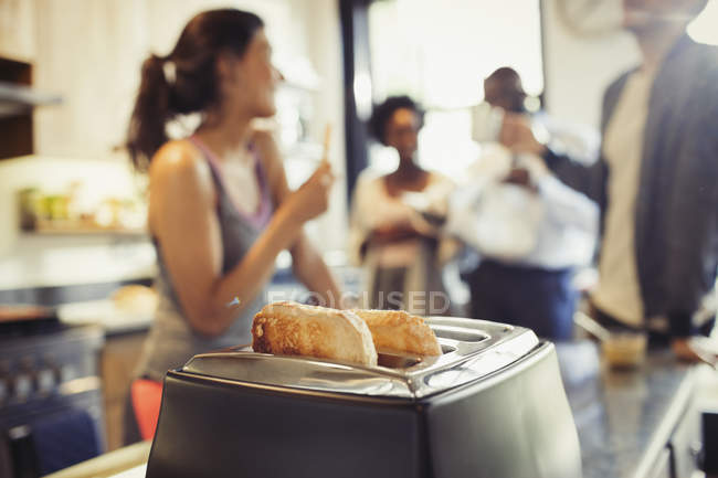 Compañeros de cuarto amigos hablando detrás de tostadas en tostadora en la cocina - foto de stock