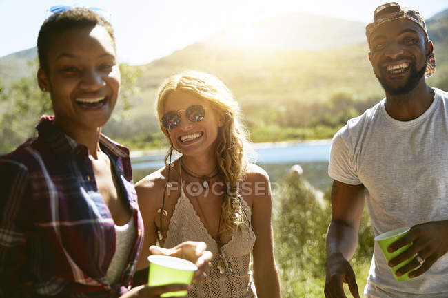 Portrait enthusiastic young friends drinking at sunny summer riverside — Stock Photo