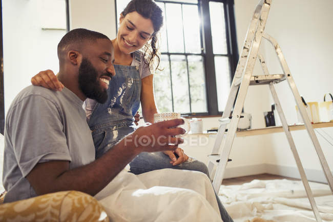 Cariñosa pareja joven bebiendo café y pintando sala de estar - foto de stock
