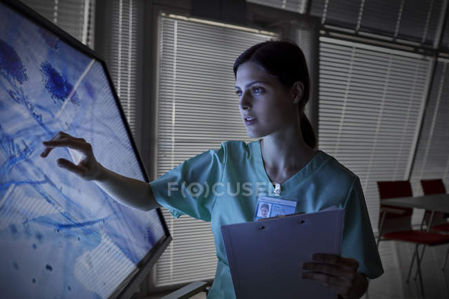 Серйозна жіноча медсестра за допомогою монітора комп'ютера з сенсорним екраном, перегляд слайда мікроскопа — стокове фото