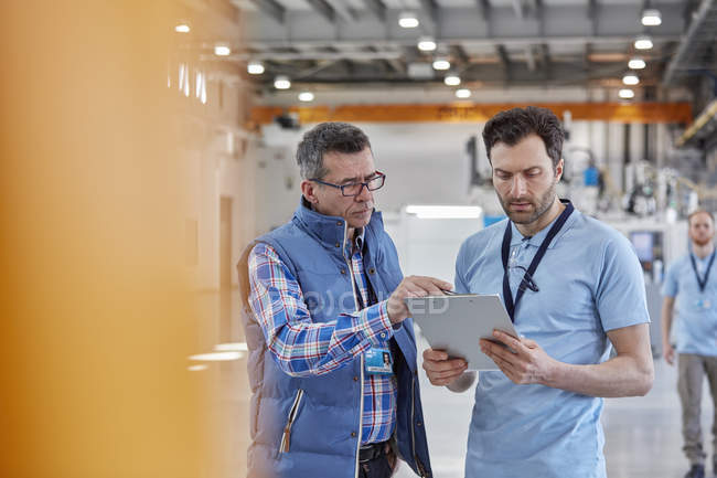 Male worker and supervisor with clipboard talking in factory — Stock Photo