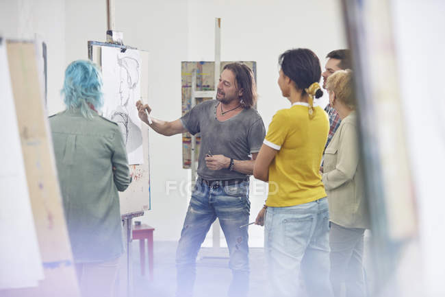 Estudiantes escuchando al instructor dibujando en el caballete en el estudio de clase de arte - foto de stock