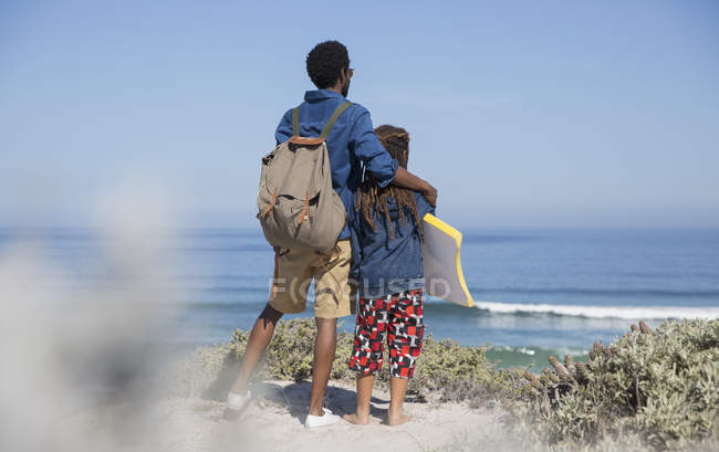 Батько і дочка з дошкою бугі дивиться на океан на сонячному літньому пляжі — стокове фото