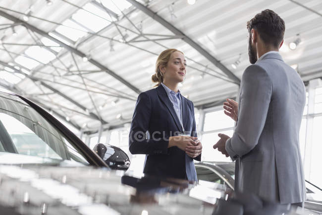 Car saleswoman talking to male customer in car dealership showroom — Stock Photo