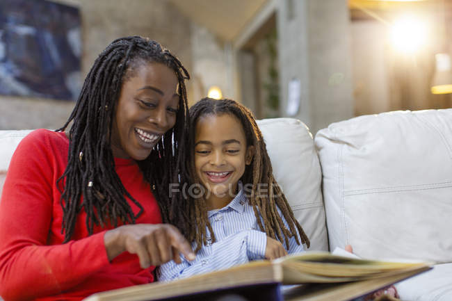 Усміхнена мати і дочка дивляться фотоальбом на дивані — стокове фото