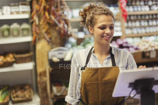 Cajero femenino usando la caja registradora de pantalla táctil en la tienda de comestibles - foto de stock