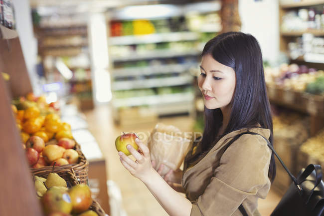 Mujer joven de compras, examinando manzana en la tienda de comestibles - foto de stock