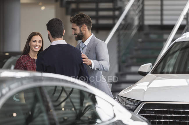 Car salesmen talking to female customer in car dealership showroom — Stock Photo