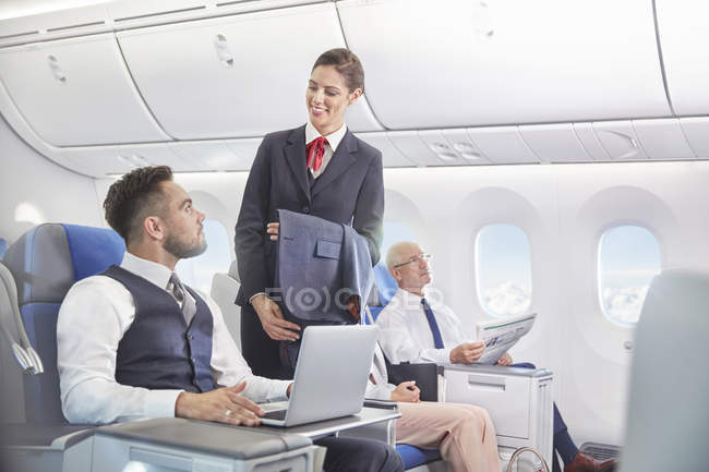 Flight attendant talking with businessman working at laptop on airplane — Stock Photo