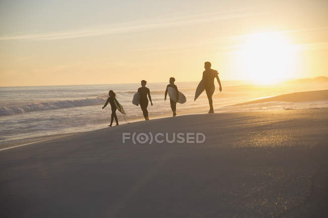 Silhouette family surfers walking with surfboards on sunny summer sunset beach — Stock Photo