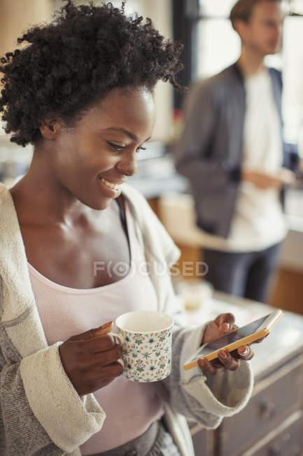 Mujer sonriente bebiendo café, mensajes de texto con teléfono inteligente - foto de stock