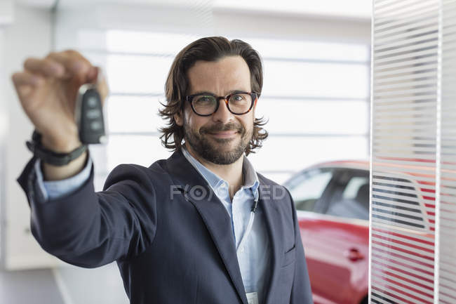 Portrait confident car salesman holding, showing car key in car dealership showroom — Stock Photo