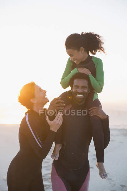 Famille heureuse en combinaison humide sur la plage de coucher de soleil d'été — Photo de stock